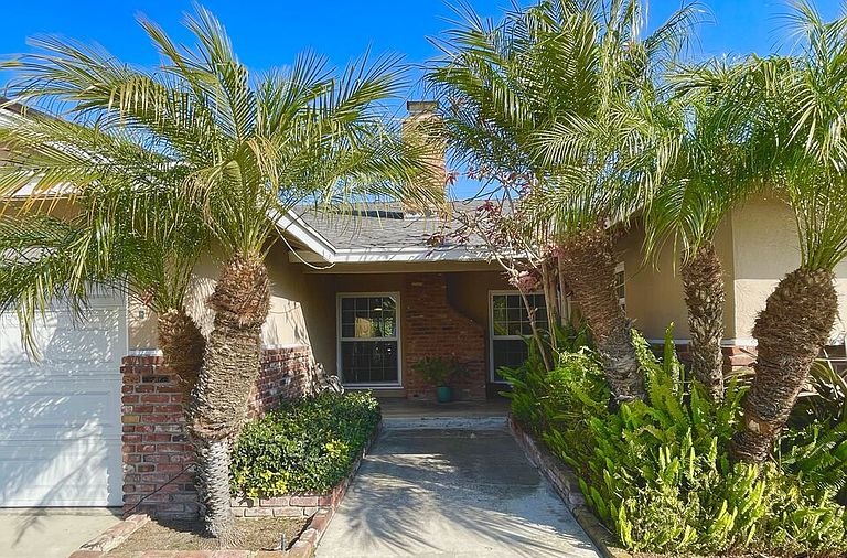 Front entry walkway at 16622 Tiber Ln lined with mature palms and brick planter walls leading to the covered front door