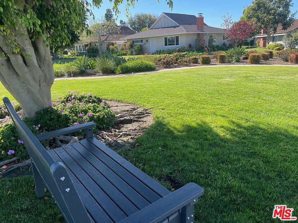Restful park-like view from a bench under a tree across an open lawn toward neighboring rooftops, suggesting the walkable parks adjacent to the neighborhood